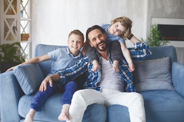 Dad with two young kids smiling on couch after family dentistry treatment, Downey CA