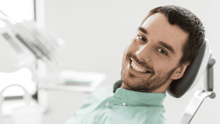 Man sitting in dental chair smiling after dental bonding treatment, downey ca